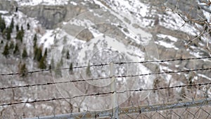 Panorama Focus on security chain link fence with barbed wires against on snowy hill slope