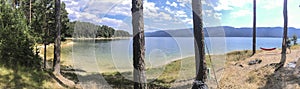 Panorama of forest and mountain lake. Hammock hooked on two pine trees