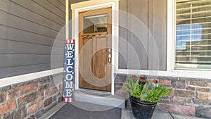 Panorama frame Brown front door with glass pane and Welcome sign against gray and stone wall