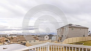 Panorama frame Brown wooden deck with white railing overlooking yard homes and cloudy sky