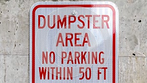 Panorama frame Close up of a sign that reads Dumpster Area No Parking against a concrete wall