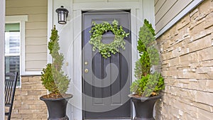 Panorama frame Gray front door of a home with green wreath and flanked by tall potted plants