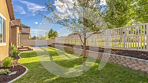 Panorama frame Home backyard with vibrant lawn and raised planting bed along white picket fence