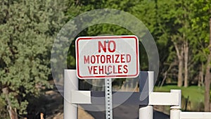 Panorama frame No Motorized Vehicle sign against a white gate and narrow road on a sunny day