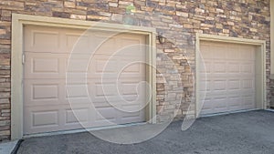 Panorama frame White garage doors of a home against exterior wall covered with stone bricks