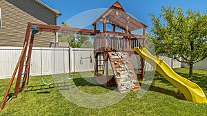 Panorama frame Wooden playground structure with yellow plastic slide swings and climbing wall