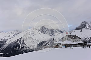 Panorama of French Alps with mountain ranges covered in snow and clouds and with mountain hut in winter