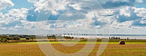 Panorama of hay bales on a farm along the ocean with the Confederation Bridge in the background