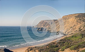 Panorama image of a beach or bay on the atlantic ocean with sand, grass, waves, high rocks and a blue sky