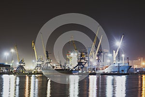 Panorama image of the illuminated cargo port in Novorossiysk, Russia at night with container terminals, cargo ship and cranes and
