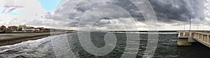 Panorama from the jetty to rough sea with scenic sky covered by clouds ready for the rain at distance a man alone looking the sea