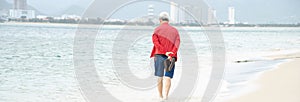 Panorama Korean man walking barefoot along white sandy beach shoreline with downtown Nha Trang skylines high rise buildings