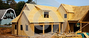 Panorama L shaped wooden house with gabled dormer roof under construction, oriented strand board OSB plywood sheeting envelope in