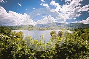 Panorama of a lake with green vegetation around. Natural basin with forest and mountains.