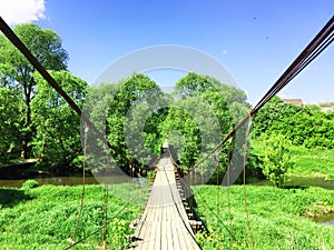 panorama landscape, forest river among green fields above it a wooden suspension bridge, on a summer day with stunning