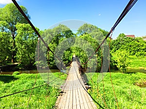 panorama landscape, forest river among green fields above it a wooden suspension bridge, on a summer day with stunning