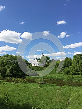panorama landscape among green fields on a summer day with stunning white clouds and blue sky, white ancient church