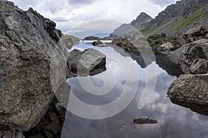 Panorama landscape with a lake in the mountains, huge rocks and stones on the coast and reflection of clouds