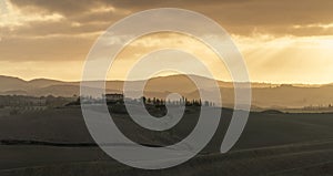 panorama landscape of rolling hills in Tuscany at sunrise with a cypress alley leading to a country estate in the distance