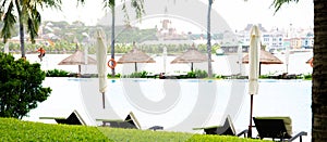 Panorama large ocean view swimming pool with life guard, lounge chairs, beach umbrella, coconut palm trees and waterfront theme