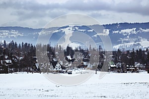 Panorama at the little tourist village in the winter, in the background forest, mountain and ski slope with ski lifts
