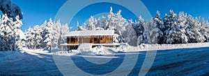 Panorama with a log cabin covered in a snowy forest