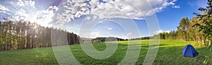 Panorama of the lush green spring meadows, tent and trees