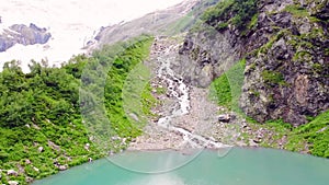 Panorama of mountain lake in clear weather from altitude with turquoise water and snow.