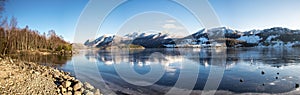 Panorama of nearly frozen Oltedalsvatnet lake and coastline with mountains peaks covered by snow during winter season