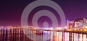 Panorama on night town with reflection of colored lights on the water surface.