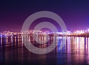 Panorama on night town with reflection of colored lights on the water surface.