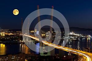 Panorama of night Vladivostok in the full moon. Golden bridge.