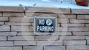 Panorama No Parking sign on a stone brick retaining wall topped with snow in winter