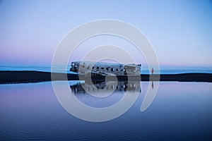 Panorama pond lake reflection of Solheimasandur DC3 airplane wreck crash site on black rock volcanic ashes beach Iceland