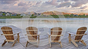 Panorama Puffy clouds at sunset Four wooden lounge chairs facing the reflective Oquirrh Lake at