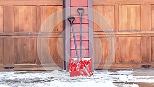 Panorama Red shovels on snowy driveway against wall and wooden garage doors of home