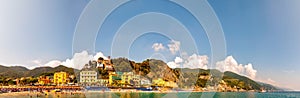 Panorama of rocky marina, clear water of Ligurian Sea, sea ships, beach full of people, waterfront buildings in Monterosso Al Mare