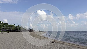 Panorama of the sandy beach with chaise lounges and sunshades in the tropical resort. Bali. Indonesia