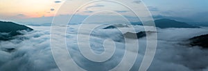 Panorama of sea of clouds around mountain peaks at sunrise