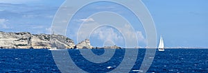 Panorama of the sea and rocks on a Sunny day. Sailing yacht with a white sail, copy space