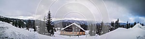 Panorama shot -Winter view overlooking a lodge in the mountains surrounded by evergreens and snow on a cloudy day, in Ranca resort