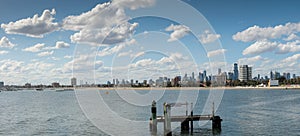 panorama showing City of Melbourne on the horizon seen from St Kilda pier looking over old timber pylons in the bay or cove on