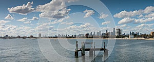 panorama showing City of Melbourne on the horizon seen from St Kilda pier looking over old timber pylons in the bay or cove on