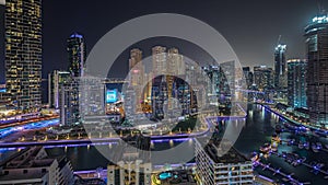 Panorama showing Dubai Marina with several boat and yachts parked in harbor and skyscrapers around canal aerial night