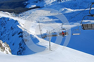 Panorama of ski resort, slope, people on the ski lift, skiers on the piste among white snow pine trees