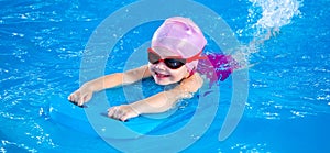 Panorama of Smiling little girl learning to swim in pool with flutterboard during swimming class