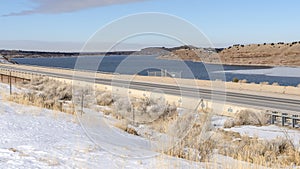 Panorama Snow covered terrain along a road overlooking mountain and lake in winter