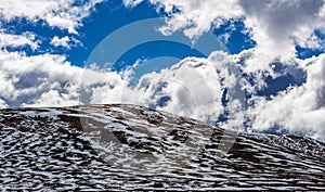 Panorama of Snow patches on mountains and fluffy clouds on bright sunny day