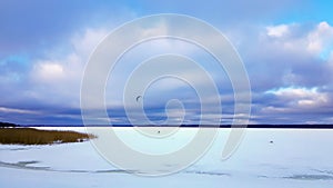 Panorama of snowy lake with lonely sportsman doing winter kiting