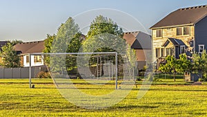 Panorama Soccer goal on vast green grassy field in front of houses viewed on a sunny day